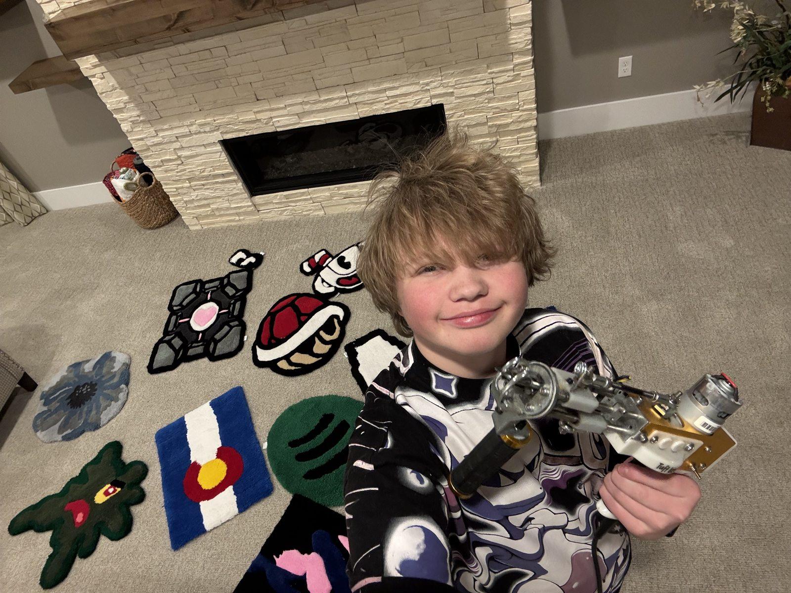 Caleb smiling, holding his tufting gun, with finished rugs laid out on the floor around him