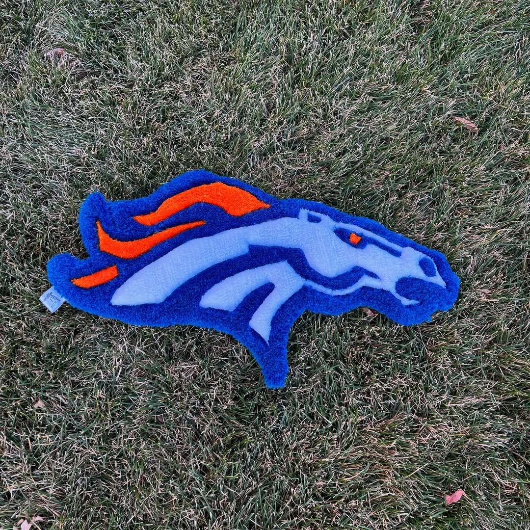 Hand-tufted blue and orange horse-head rug lying on grass