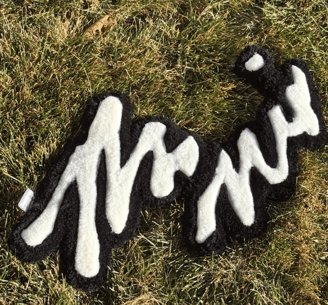 Hand-tufted white script lettering rug on a black base, photographed on grass