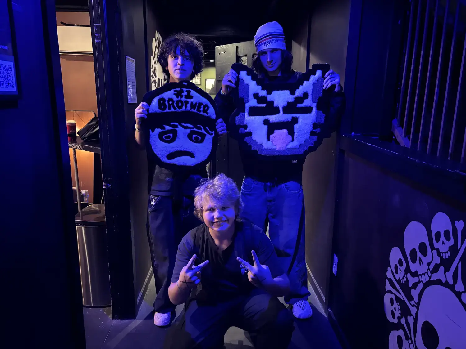 Three people posing with the finished rugs in a blue-lit venue