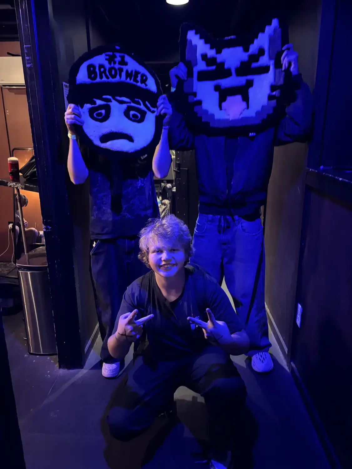 Three people under blue venue lights holding two hand-tufted character rugs