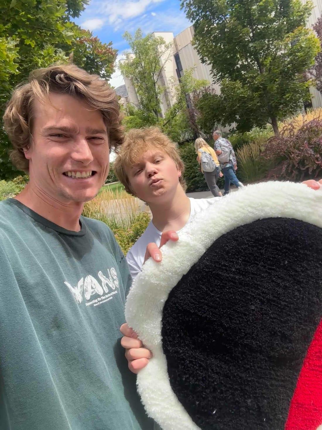 Two people outdoors holding up the finished round Skategrounds rug
