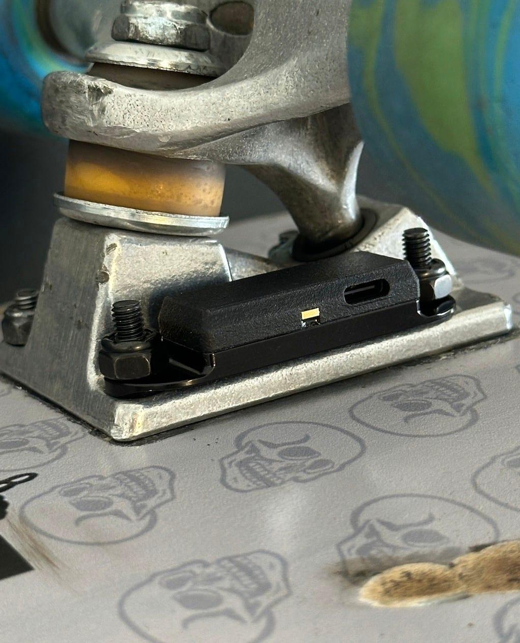 Close-up of the Skategrounds sensor bolted under a skateboard truck baseplate, USB-C port visible