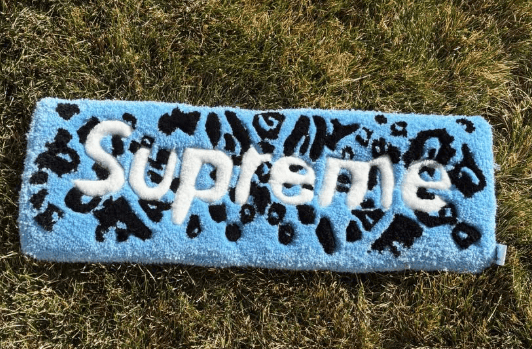 Hand-tufted pale blue box-logo rug with black leopard print lettering, laid on grass